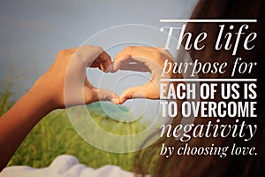 Inspirational quote - The life purpose for each of us is to overcome negativity by choosing love. With girl making hands love sign