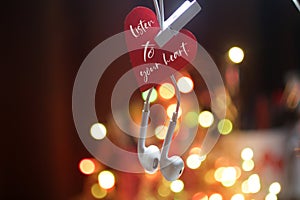 Inspirational quote - Listen to your heart. With red heart hanging on white earphone on colorful bokeh lights bakground.