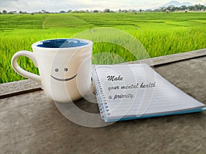 Inspirational quote - Make your mental health a priority. Physiology text message on spiral notebook with smiling cup of tea.