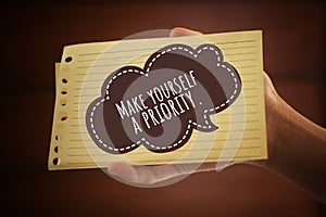 Inspirational quote - Make yourself a priority. With paper sign in hand. Self love and care concept on brown background