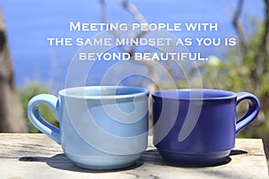 Inspirational quote - Meeting people with the same mindset as you beyond beautiful. With cups of coffee on blue outdoor backgroud.