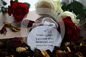 Inspirational quote - Never ignore a person who loves you and cares for you. Motivational note on paper tag label with roses.