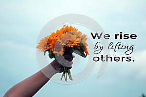 Inspirational quote - We rise by lifting others. Young woman showing bouquet of sun flowers in hand against blue sky background. photo