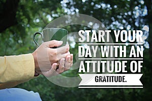 Inspirational quote - Start your day with an attitude of gratitude. With person holding a cup of tea or coffee in hands on green