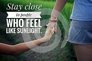 Inspirational quote - Stay close to people who feel like sunlight. With couple holding hands in the field on green paddy plants.