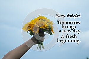 Inspirational quote - Stay hopeful. Tomorrow brings a new day. A fresh beginning. With hand holding beautiful bouquet of sunflower