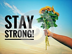 Inspirational quote - Stay strong.  With hand holding bouquet of sunflowers against bright blue sky background.