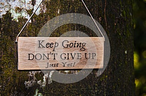 Inspirational quote text on wooden banner - Keep going, don't give up. With tree and blurred nature background.