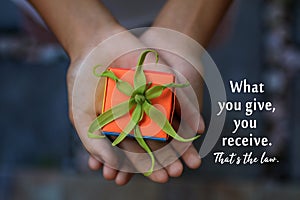 Inspirational quote - What your give, you receive. That is the law. With a small cute gift box in young woman hands.