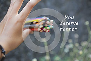 Inspirational quote - You deserve better. With an illustration background of young woman hand release a bunch of colored pencils.