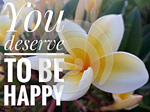 Inspirational quote - You deserve to be happy. On background of beautiful white and yellow Bali frangipani flower plant blossom.