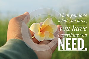 Inspirational quote - When you love what you have, you have everything you need. With hand holding Bali frangipani flower.