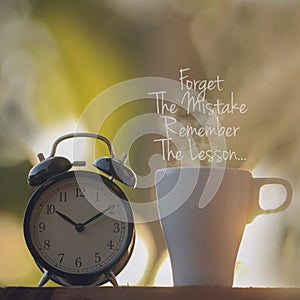 Inspirational quotes - Forget the mistake. Remember the lesson.Black alarm clock and a cup of coffee on the morning.