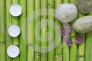 Inspirational scene with three candles aligned, stones and gemstones on a natural green bamboo background.