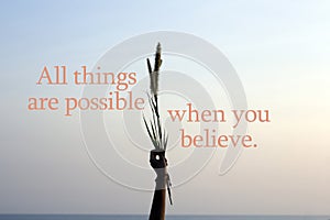Inspirational words - All things are possible when you believe. With arm of young woman raised holding grass flower plant in hand