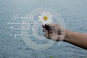 Inspirational words - No beauty shine brighter than that of a good heart. With person holding a flower in hand on blue background.