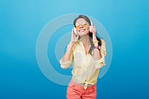 Inspired asian female model in pink wristwatch and green bracelet listening music on blue background. Indoor photo of