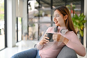 Inspired Asian woman holding a coffee cup, looking out window and relaxing in the coffee shop