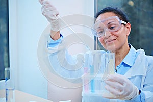 Inspired Hispanic woman lab assistant, scientist chemist using lab dropper dripping few chemical reagent into test tubes