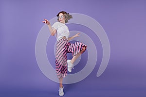 Inspired jocund girl in sneakers dancing on purple background. Gorgeous young female model with dar