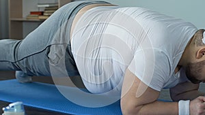 Inspired overweight sportsman practicing plank exercise on mat, fitness program