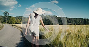 Inspired woman walk on road along wheat field and touch harvest of rye