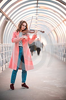 Inspired young woman in pink coat playing a fiddle on the overhead passage