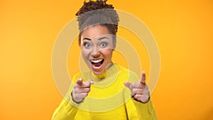 Inspired young woman pointing hands in camera on yellow background, motivation