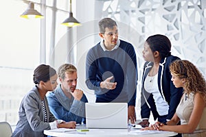 Inspiring his team with new business ideas. a team of businesspeople working on a laptop together at a table in the