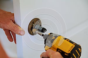 Installation of door lock using a screwdriver to. Carpenter at lock installation with electric drill into wood door.