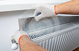 Installation of a foil thermal insulation on the wall behind the heating radiator at home.