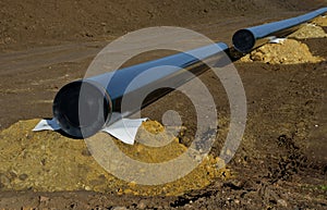 Installation of gas pipelines in field. excavated topsoil hiding route. black pipe is supported by piles of soil and is welded abo