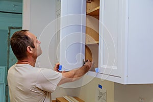 Installation kitchen. Worker installs doors to kitchen cabinet. photo