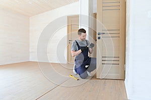 Installation of a lock on the front wooden entrance door. Portrait of young locksmith workman in blue uniform installing
