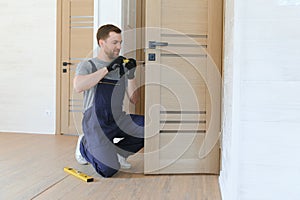 Installation of a lock on the front wooden entrance door. Portrait of young locksmith workman in blue uniform installing