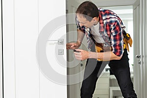 Installation of a lock on the front wooden entrance door. Portrait of young locksmith workman in blue uniform installing