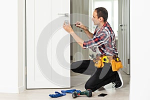 Installation of a lock on the front wooden entrance door. Portrait of young locksmith workman in blue uniform installing