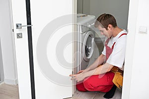 Installation of a lock on the front wooden entrance door. Portrait of young locksmith workman in blue uniform installing