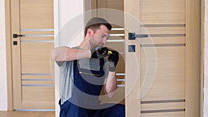 Installation of a lock on the front wooden interior door. Portrait of young locksmith workman in uniform installing knob