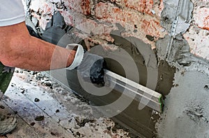 Installation of metal guiding beacons for filling and leveling of walls in the repair. Hand covers the wall with plaster