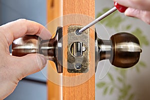 Installation of new brass door handles with a latch in a wooden interior door, a locksmith's hand with a screwdriver