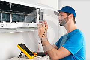 Installation service fix repair maintenance of an air conditioner indoor unit, by cryogenist technican worker with multimeter