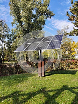 An installation with solar panels is installed in a city park on the grass to illuminate the park with lamps at night