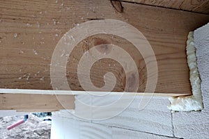 Installation of wooden beams of roof frame with spray foam on a house wall under construction