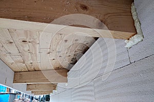 Installation of wooden beams of roof frame with spray foam on a house wall under construction