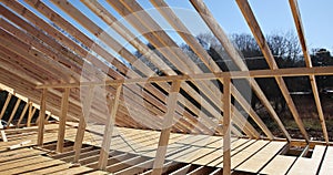 Installation of wooden roof beams over an already built stick home with framework trusses on the construction site.