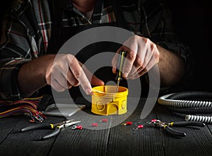 Installing a cable or wire to yellow junction box. Close-up of hands of a master electrician during work in workshop