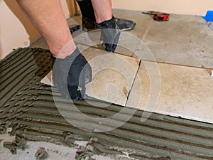 Installing ceramic floor tiles - placing the tile into the adhesive material bedding, closeup