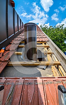Installing external chimney trough a house roof with roof tiles.