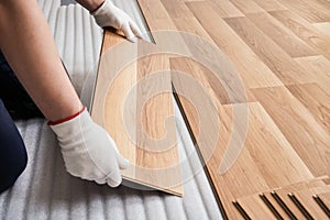 Installing laminated floor, detail on man hands with white gloves fitting wooden tile, over white foam base layer